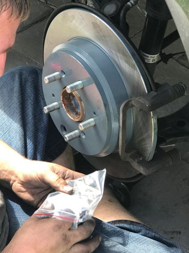 Person holding parts near a car brake rotor.