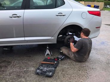 Man repairing a car wheel with tools on wet pavement.