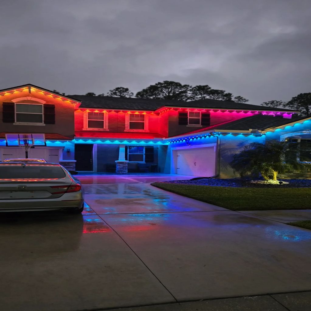 Two-story house decorated with vibrant multicolored string lights at night.