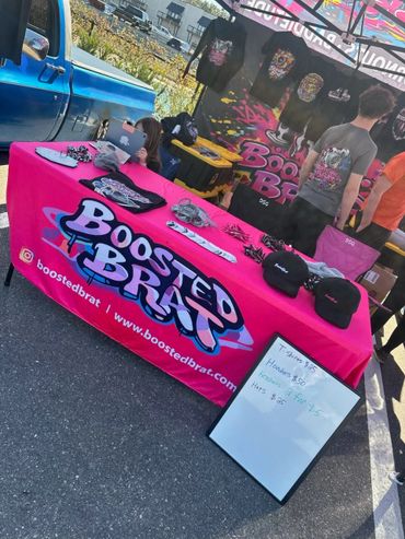 Outdoor merchandise booth selling Boosted Brat apparel and accessories.
