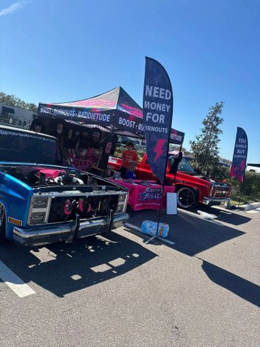 Car show booth with custom trucks and banners asking for support and sales.