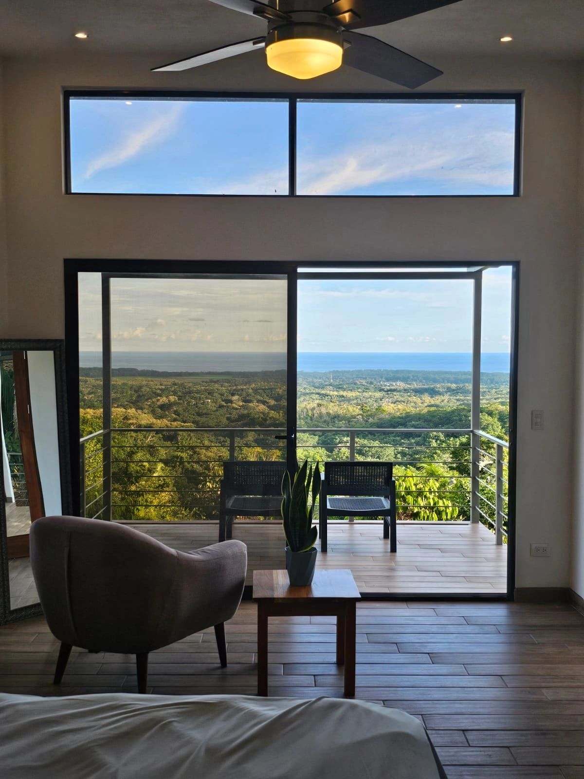 Modern room with balcony overlooking lush greenery and ocean.