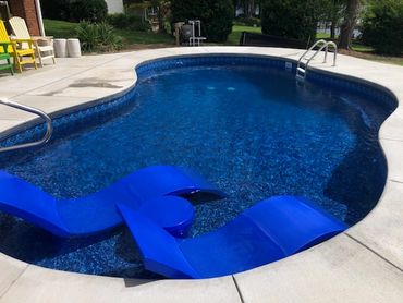 Curved swimming pool with two blue lounge chairs.
