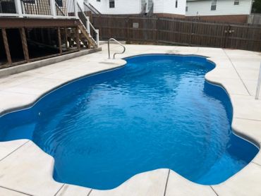 Empty backyard swimming pool with concrete surroundings.