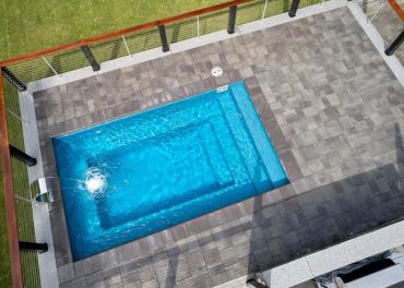 Modern outdoor pool with water feature and gray tiles.