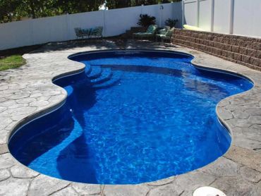 Clear, blue backyard swimming pool with stone patio.