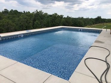 Empty outdoor swimming pool surrounded by greenery.