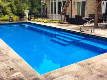 Clean backyard pool with patio furniture and stone tiles.