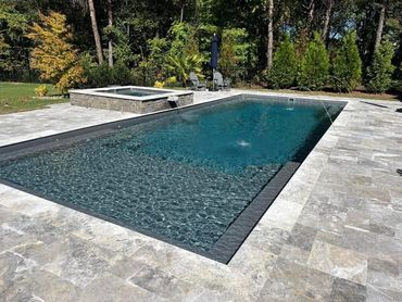 Modern backyard swimming pool with hot tub and trees.