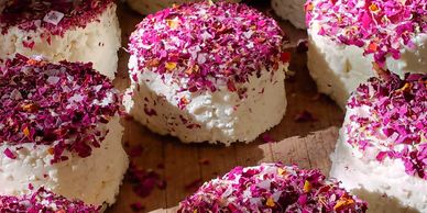 Soft white cheese rounds topped with pink flower petals on a wooden surface.