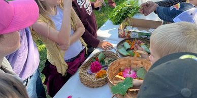 Children and adults gather around a table with colorful flowers and leaves outdoors. One of our Farm Tours for school children