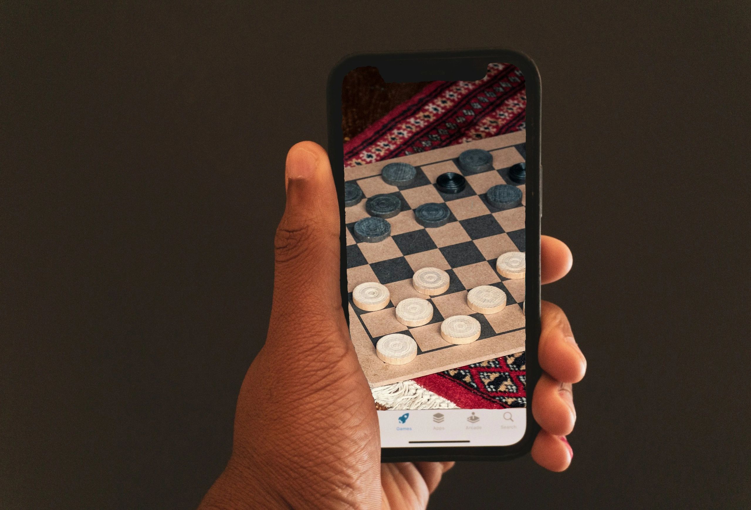 Black men sit in classy room playing on mobile app, cash on table, traditional checkers game middle