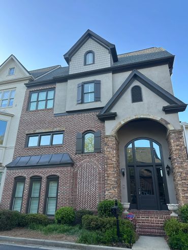 Elegant multi-story house with brick and stone facade under clear blue sky.