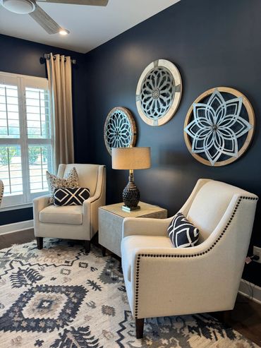 Cozy sitting area with beige chairs, patterned cushions, and artistic wall decor on a dark blue wall.
