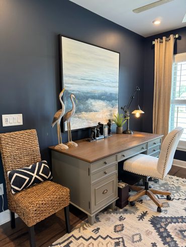 Cozy home office with a wooden desk, decorative birds, and a woven chair against navy walls.