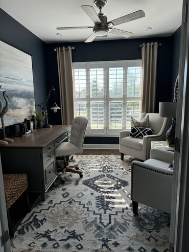 A cozy home office with navy walls, a wooden desk, and light armchairs.