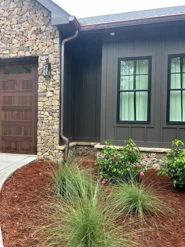 Stone and wood house exterior with landscaped garden bed and green plants.