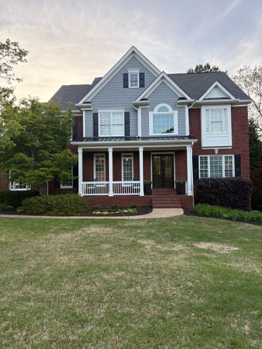 A beautiful two-story house with a mix of brick and blue siding, surrounded by greenery.