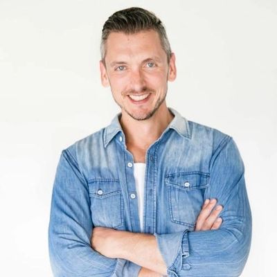 Smiling man in a denim shirt with arms crossed against a white background.