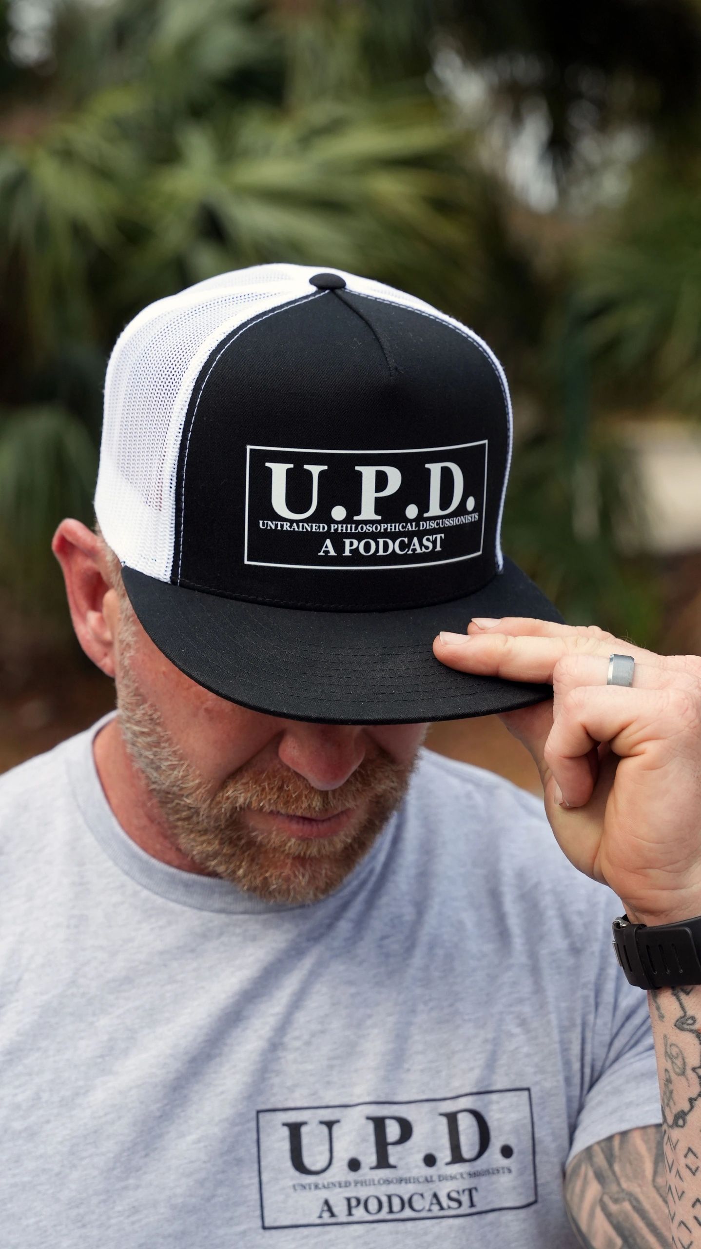 Man wearing a black and white cap and gray t-shirt promoting U.P.D. podcast.