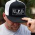 Man wearing a black and white cap and gray t-shirt promoting U.P.D. podcast.
