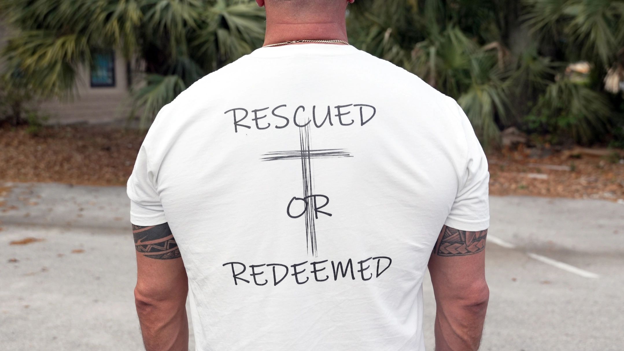 Man wearing a white shirt with 'Rescued or Redeemed' and a cross design on the back.