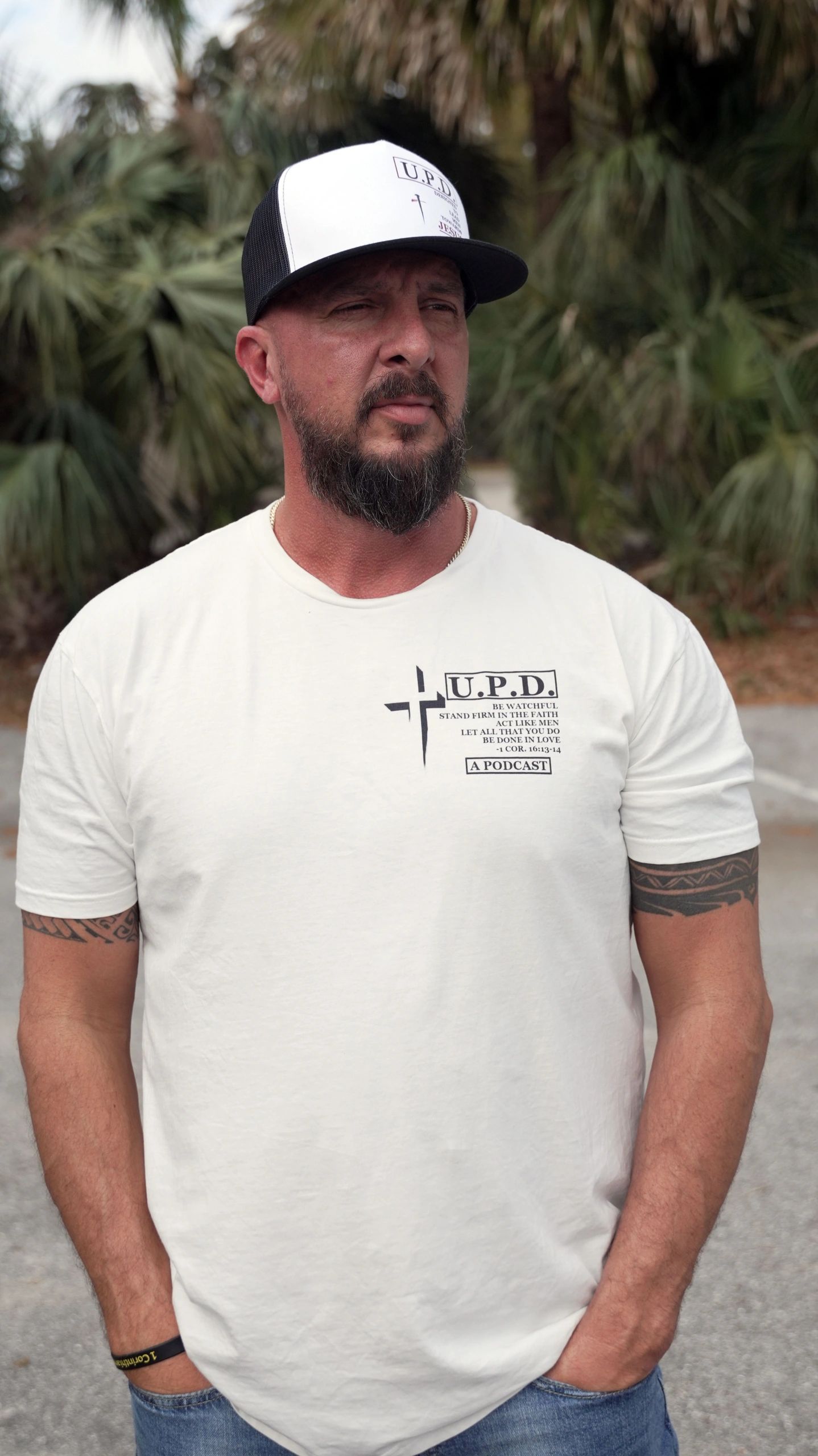 Man wearing a white U.P.D. podcast t-shirt and cap with tattoos on arms.