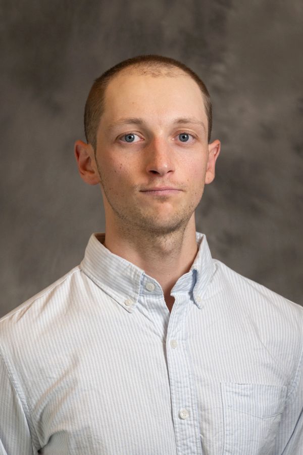 Portrait of a young man in a light striped button-up shirt against a gray backdrop.