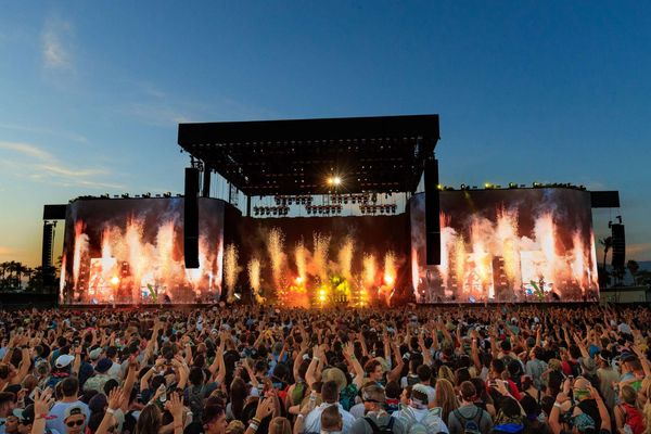Crowd enjoying a vibrant outdoor concert with pyrotechnics at sunset.