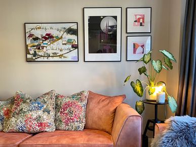 Velvet blush coulored sofa with gallery wall of original artworks, colourful soft cushions and plant