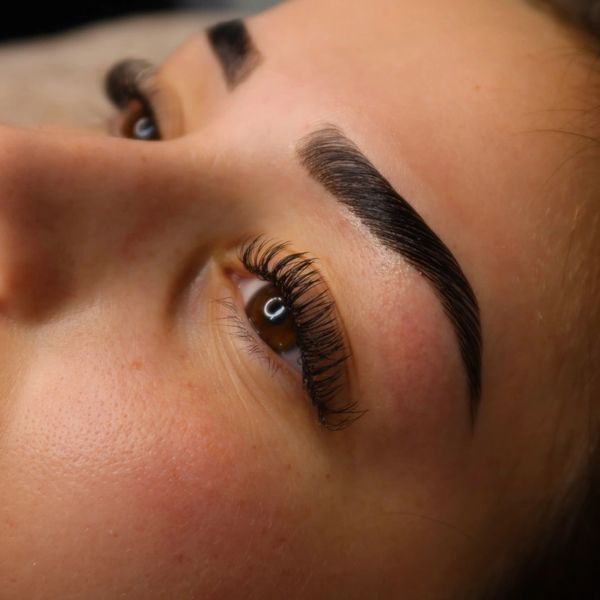 Close-up of a person's eye with thick, well-groomed eyebrows and long eyelashes.
