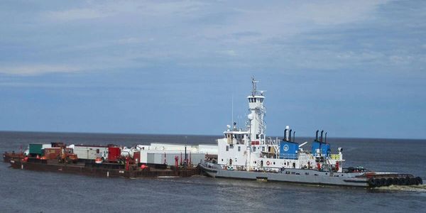 Tugboat towing a large barge on a calm sea under a partly cloudy sky.