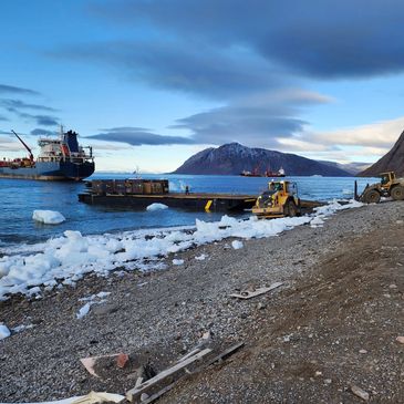 Cargo ships docked near an icy shore with construction vehicles working on the beach.
