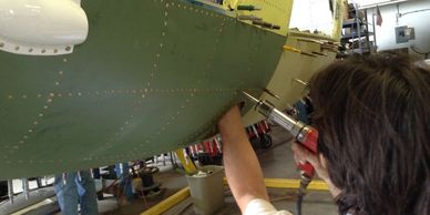 A technician performs rivet work on the fuselage of an MD 530FF, serial 0064FF.