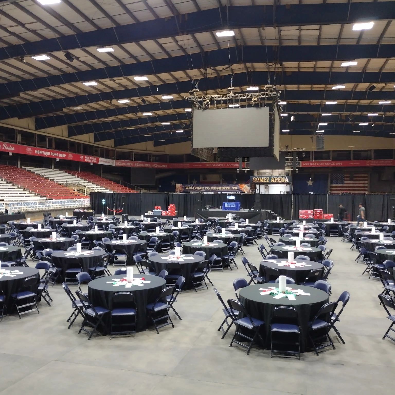 Empty round tables with black tablecloths set in a large indoor arena.