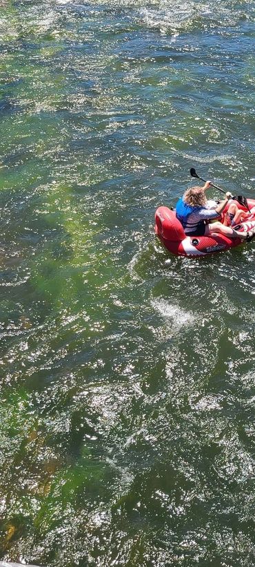 Two people paddling a red inflatable kayak on a river surrounded by mountains and trees.