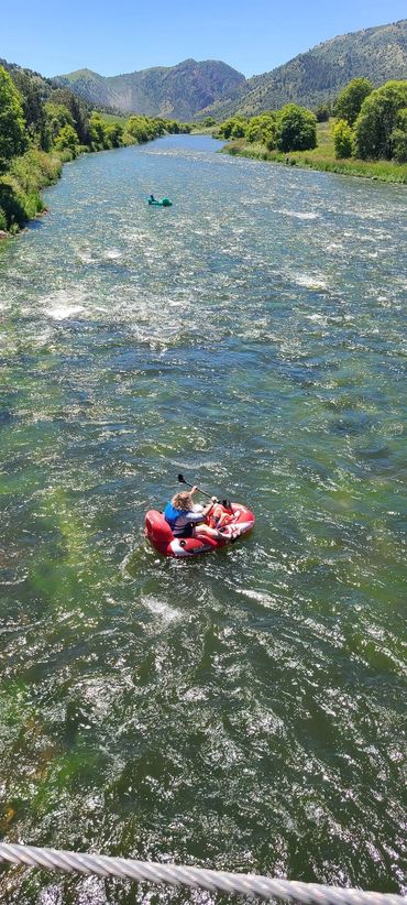 Two people kayaking on a river surrounded by green trees and mountains.
