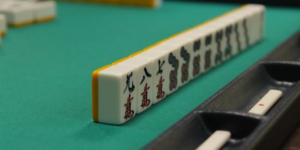 Row of Mahjong tiles on a green table with a black tray.