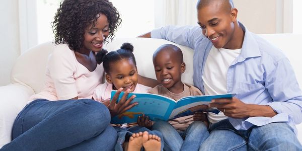 A joyful family reads a book together on a white couch.
