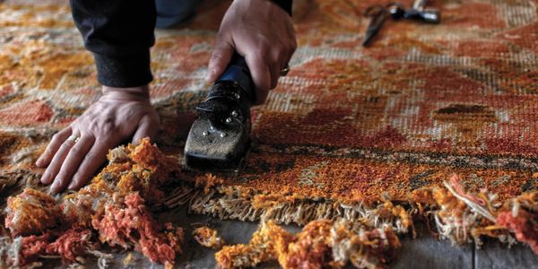 Person using a tool to repair a frayed, colorful rug.