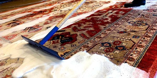 Cleaning a patterned rug with foamy soap and a squeegee tool.