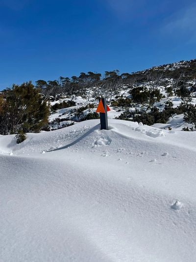 Marker post on Thark Ridge Track emerging from a deep snow drift under a blue sky