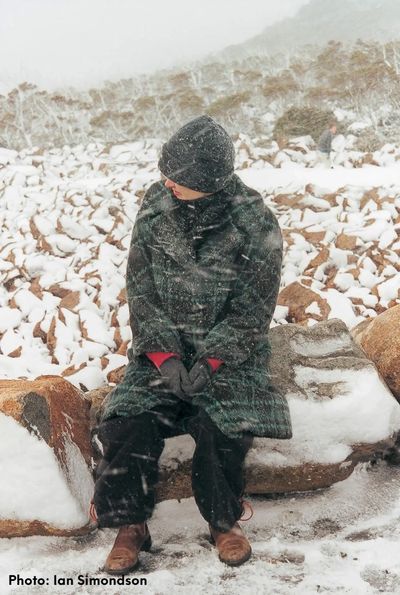 Lady sitting in a snow storm on some boulders