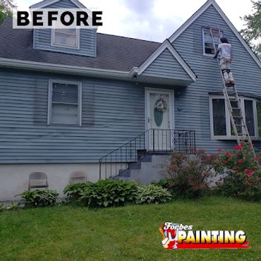 A man prepares to paint a blue house, standing on a ladder.