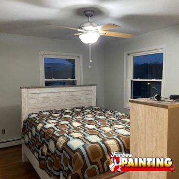 Cozy bedroom with patterned bedspread and ceiling fan in soft lighting.