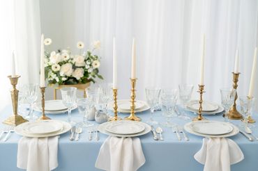 Dining table set for 6 guests with china, crystal goblets, silverware, candleholders and flowers.