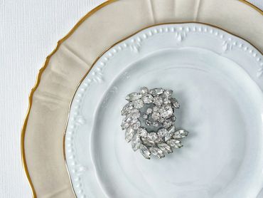 Vintage rhinestone brooch adorning a pair of mismatched white dinner and salad plates.