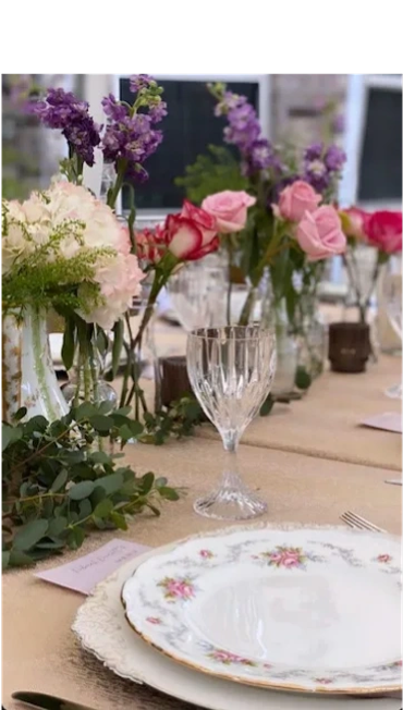 Backyard party with floral china on paper covered tables with crystal goblets and seasonal flowers.