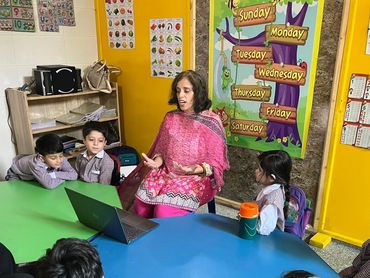 Teacher engages young students in a colorful classroom around a laptop.