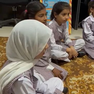 Young girls in school uniforms sitting attentively on a carpet indoors.